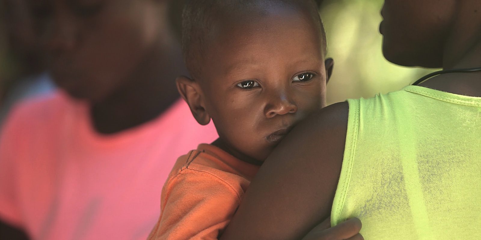 woman carries boy in orange shirt